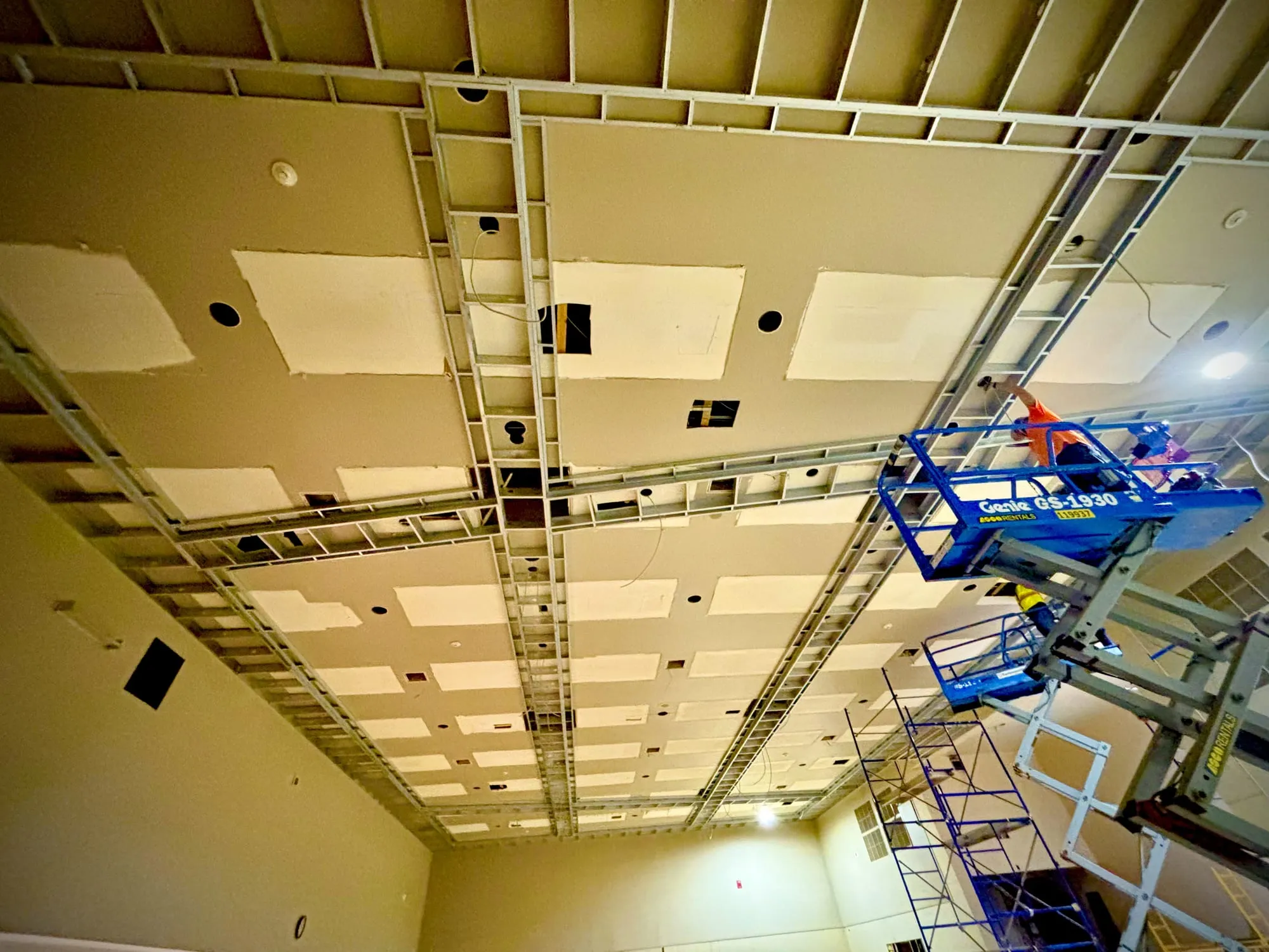 Premier Drywall crew installing a suspended drywall ceiling grid from a scissor lift